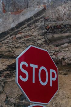 Red stop sign on the background of a destroyed brick wall close up