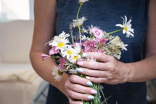 a young woman with a beautiful summer manicure holds a bouquet of wild flowers in pastel shades. High quality photo