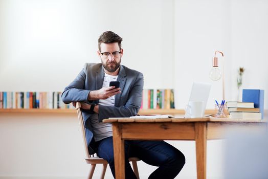 Communication is key when working remotely. a handsome young businessman sending a text message while sitting in the home office