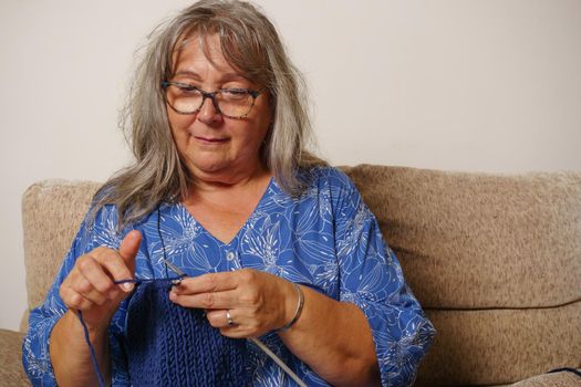 Mature white-haired woman with glasses sitting in an armchair weaving