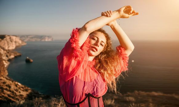 Close up shot of beautiful young caucasian woman with curly blond hair and freckles looking at camera and smiling. Cute woman portrait in a pink long dress posing on a volcanic rock high above the sea