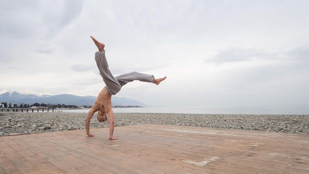 Shirtless caucasian man doing backflip on pebble beach