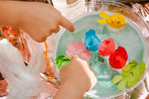 Children's hands pointing at paper flowers in a container with water. holidays and entertainment for children.