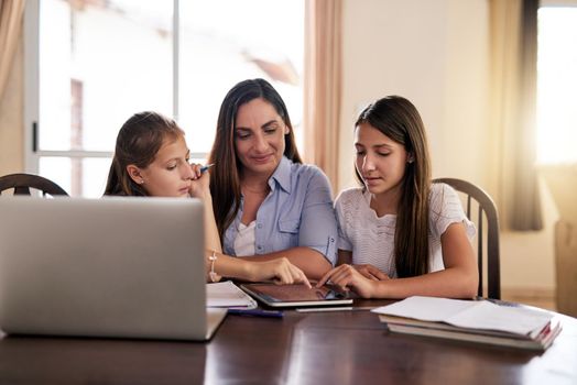 Do the two of you understand now. two cheerful young girls doing homework around a table while getting help from their mother at home during the day