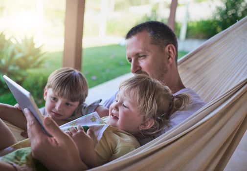 Dads always willing to watch cartoons with his kids. a father and his two little children using a digital tablet while relaxing on a hammock outdoors