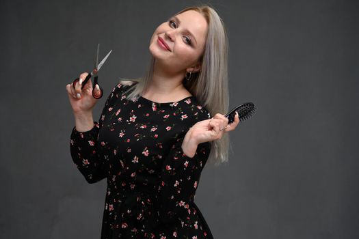 Beautiful girl with blond hair with scissors and a comb in her hands