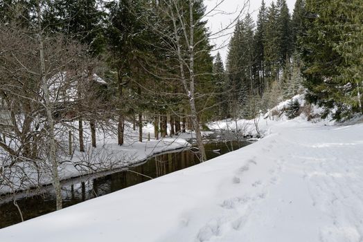 A small quiet flowing river in a snow-covered winter landscape.