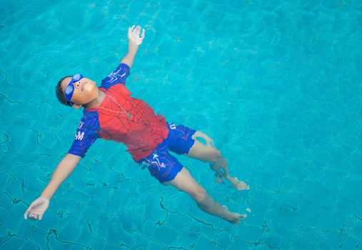 boy wearing a swimsuit and glasses swimming in the middle of the pool with a blue water background