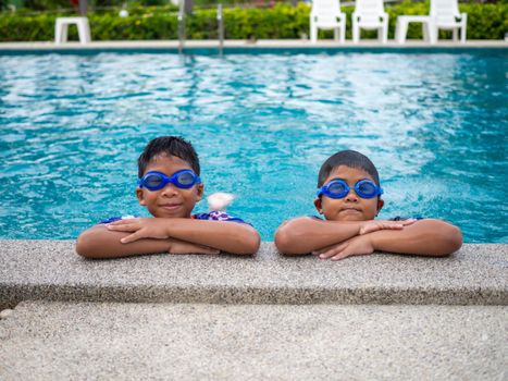 brothers wearing swimsuits and glasses Smile while perched on the edge of the pool.
