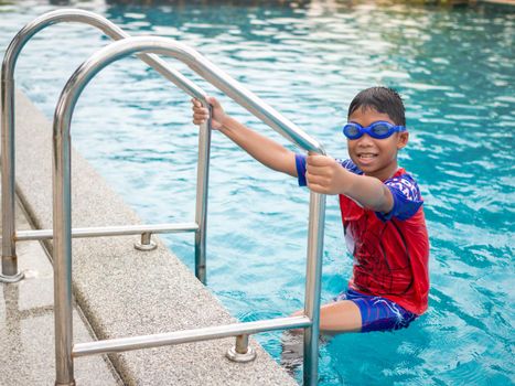 The boy wearing swimming goggles on blue pool ladder red swimsuit