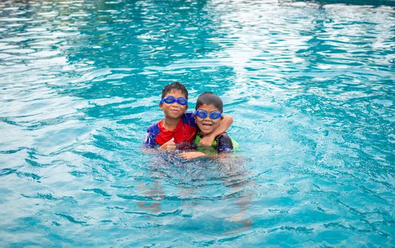 Brothers wear a swimsuit and goggles. Smile and enjoy playing in the water in the blue pool