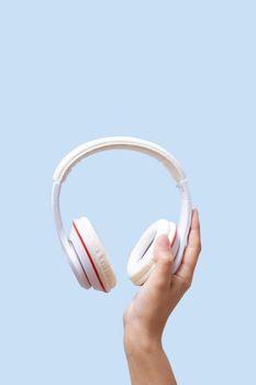 A female hand holds white headphones on a blue background. High quality photo