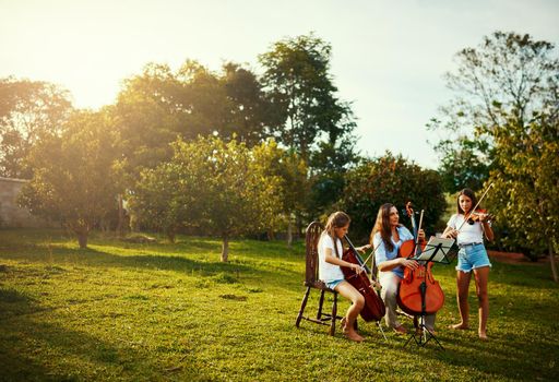 Her favourite part of the week, practicing with her girls. a beautiful mother playing instruments with her adorable daughters outdoors