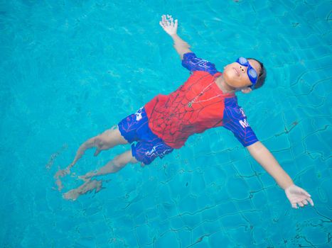 boy wearing a swimsuit and glasses swimming in the middle of the pool with a blue water background