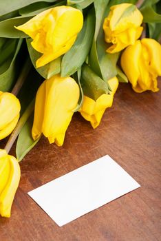 Yellow tulips with blank card on wooden boards