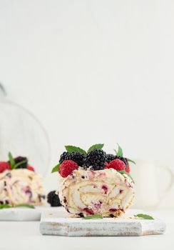 Baked meringue roll with cream and fresh fruits on a white wooden board, delicious dessert