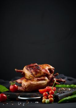 Frying carcasses of quails lie on a wooden board with vegetables, a black table