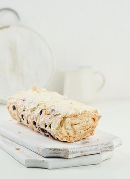 Baked meringue roll with cream and fresh fruits on a white wooden board, delicious dessert