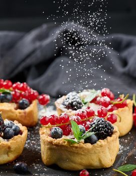 Fruit tart with red currants sprinkled with powdered sugar on a black table