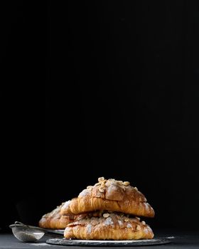 Baked croissant on a  board and sprinkled with powdered sugar, black table. Appetizing pastries for breakfast	