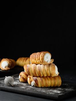 Baked tubules with whipped protein cream on a wooden board, black background