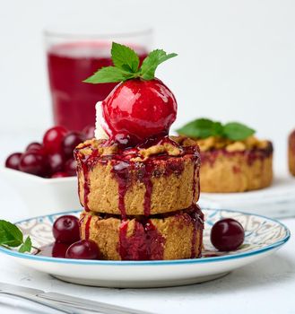 Cherry crumble pie decorated with a scoop of ice cream and drizzled with cherry sauce on a plate