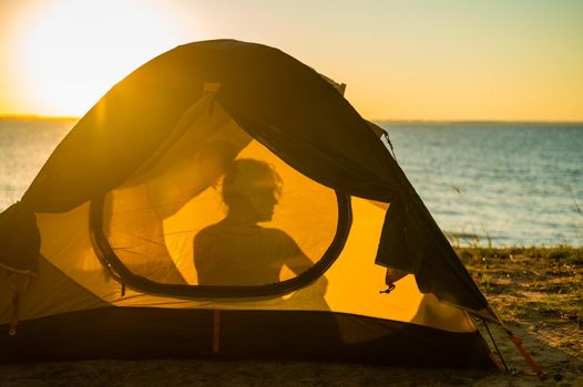 Woman and dog in a tourist tent at sunset. Camping with a pet.