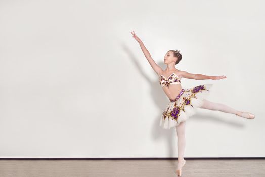 A young ballerina performs ballet exercises in the studio against a white background