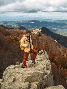 Happy traveler is standing on rock and enjoying the journey. Scenic landscape with view to the autumn forest and mountains
