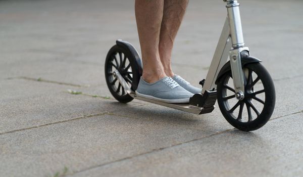 Man feet on scooter close up wearing in a sneakers shoes. Scooter with big wheels man having a ride on the streets or park after work outdoors. No face visible. Selective focus on feet.