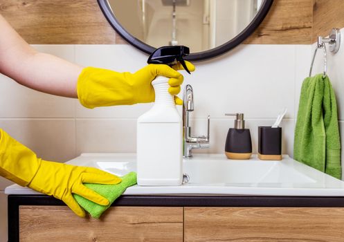close-up of a female hand in a protective glove holding white bottle, cleaning agent mockup, space for logo and label. Bathroom background. The concept of hygiene, cleanliness and cleaning in house
