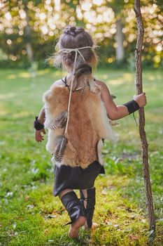 Cute baby dressed in the clothes of primitive people with combat staff.