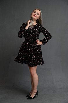 Full length portrait of a happy beautiful girl wearing dress posing while standing isolated over gray background