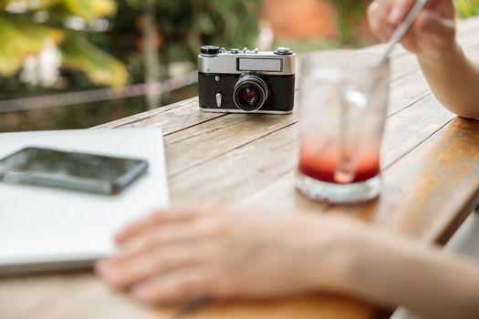 Close up of female hands holding a straw and drinking a cool drink with photo camera on the background