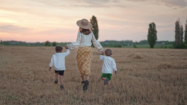 Two ukrainian boys and mother running together on open area wheat field after harvesting. Family friends holding hands. Children is our future. Nature background. Happy childhood. High quality photo