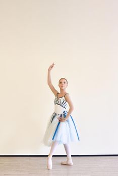 A young charming ballerina in a dress practicing ballet poses in the studio