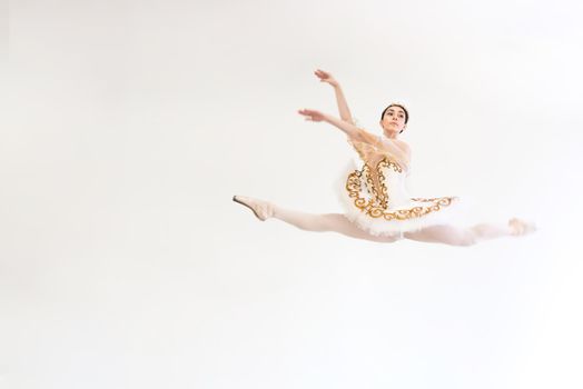 A young charming ballerina does ballet exercises in a jump against a white background