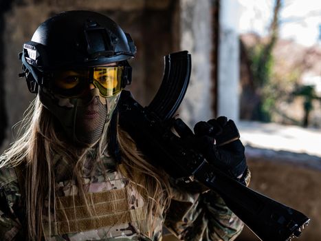 Portrait of a woman in a helmet and goggles with a machine gun in her hands. A female soldier in a camouflage uniform holds a weapon