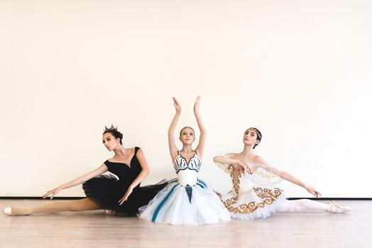 Three young ballerinas perform paired exercises against a white background in the studio