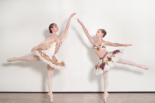 Two ballerinas young practicing ballet poses against a white background