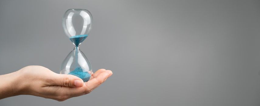 Woman holding an hourglass on a gray background. Close-up. Copy space
