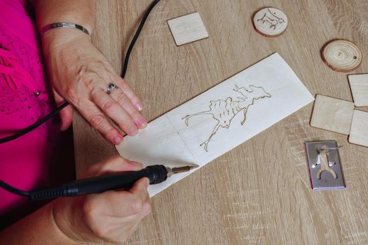 woman drawing with a pyrographer on a wooden table