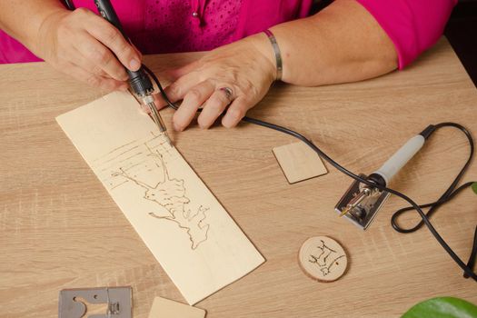 woman drawing with a pyrographer on a wooden table
