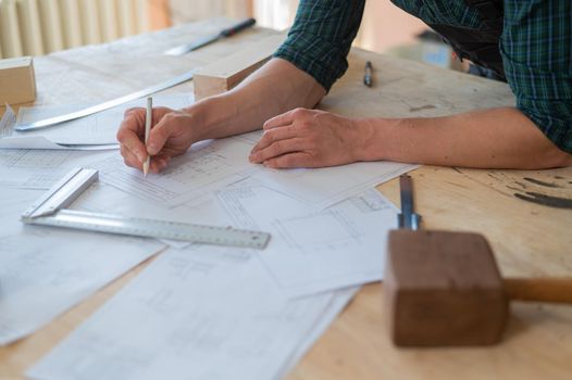 A portrait of a carpenter in goggles and work overalls draws a blueprint for a workshop