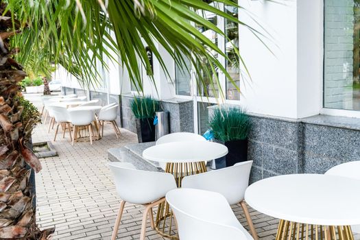 Street cafe with white chairs, green foliage around. Without people, tourism, travel