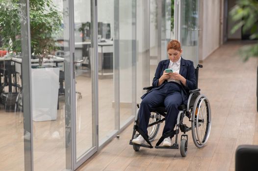 Caucasian woman using mobile phone in wheelchair at office