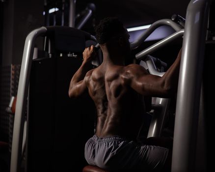 Shirtless african american man doing back exercises on a machine in the gym