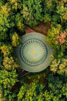 Aerial top view of Rose of Wind sign in city park. Emblem star compass wind rose with four tips made on soft rubber coating inside swings in ring form at green park, late summer. Drone view, vertical