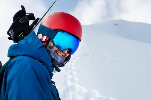 Equipped skier holding skis on his shoulder and looking directly at the camera, portrait. Man with winter equipment in the mountains at a ski resort.