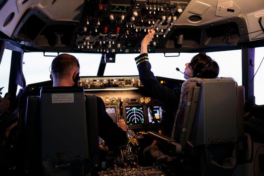 Captain and female copilot getting ready to fly plane and takeoff with dashboard navigation in cockpit command. Airline crew fixing altitude level and with control panel buttons, flying airplane.